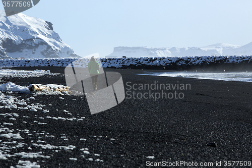 Image of Woman walks along black sand beach in Vik, Iceland