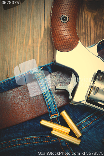 Image of silvery revolver nagant with cartridges on old blue jeans