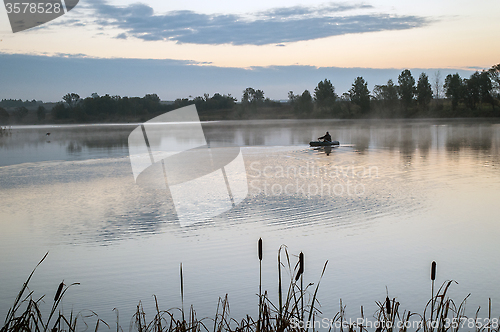 Image of A fisherman in a boat sailing in the morning mist