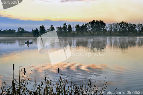 Image of A fisherman in a boat sailing in the morning mist