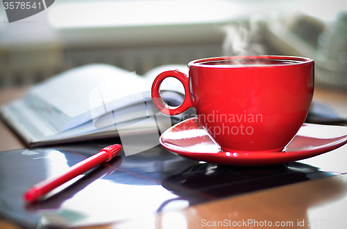 Image of Red cup of hot coffee, notepad and pencil on the desktop in the 