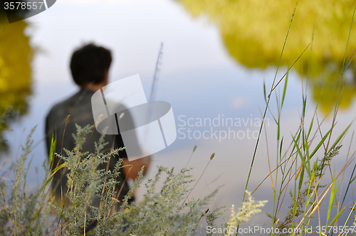 Image of Blurred silhouette of fisherman on the river on a clear summer d