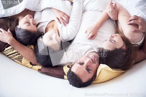 Image of handsome man in bed with three beautiful woman