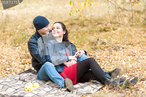 Image of Young romantic couple sits on plaid. Autumn picnic