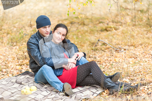 Image of Young romantic couple sits on plaid. Autumn picnic
