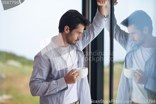 Image of relaxed young man drink first morning coffee withh rain drops on