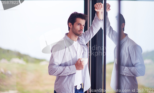 Image of relaxed young man drink first morning coffee withh rain drops on