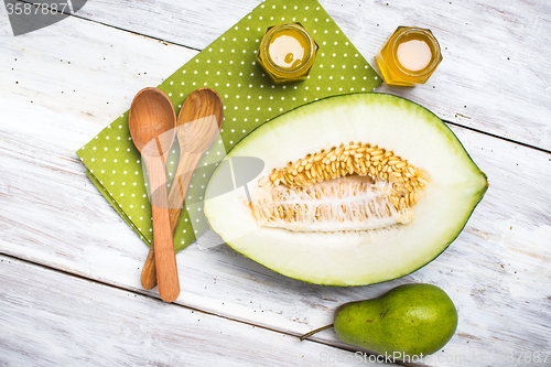 Image of Ripe melon spoons honey and pear on white wood