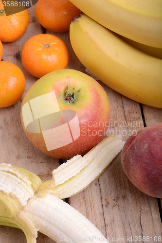 Image of Bananas apple mandarin peach on wooden background as health food concept