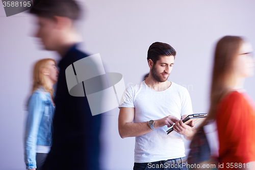 Image of student working on tablet, people group passing by