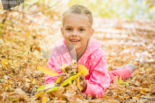 Image of Six year old girl lying on the yellow fallen leaves