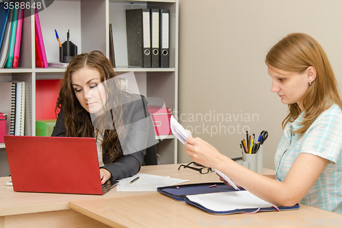 Image of The specialist works in the laptop, the visitor leafing through paper documents