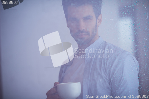 Image of relaxed young man drink first morning coffee withh rain drops on