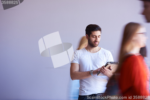 Image of student working on tablet, people group passing by