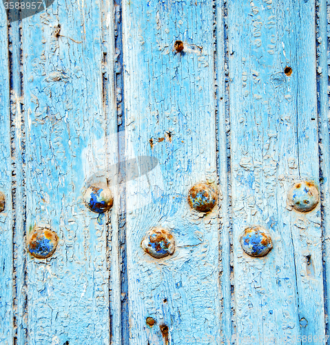 Image of dirty stripped paint in the blue wood door and rusty nail