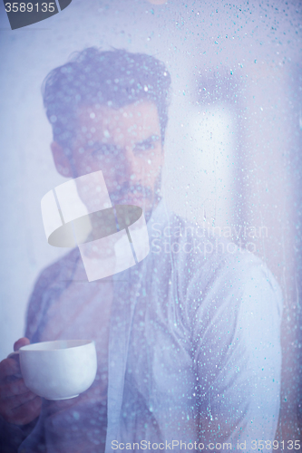 Image of relaxed young man drink first morning coffee withh rain drops on