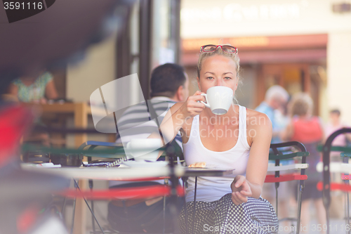 Image of Woman drinking coffee outdoor on street.