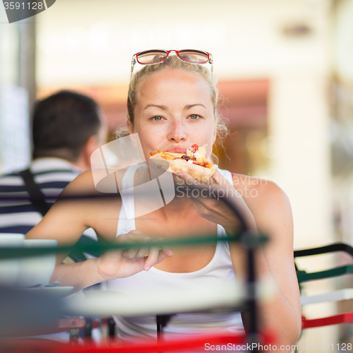 Image of Woman eating pizza outdoor in cafeteria.