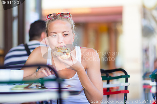 Image of Woman eating pizza outdoor in cafeteria.