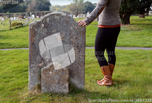 Image of Woman rests her hand thoughtfully on a headstone