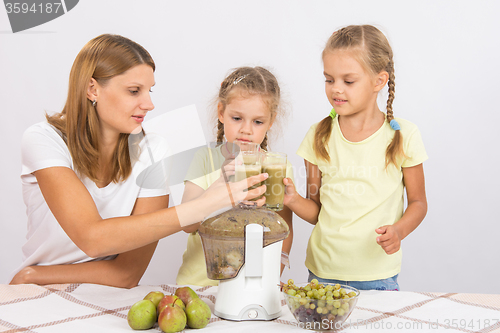 Image of Mother and two daughters knocked against each other with glasses of freshly made juice from the pears and grapes