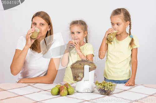 Image of Mother and two daughters drink freshly juice from the pears and grapes
