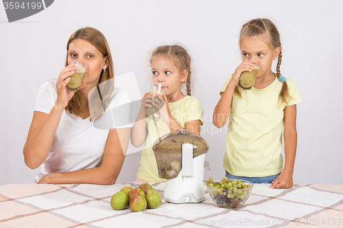 Image of Mother and two daughters taste the freshly prepared juice from pears and grapes