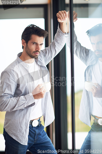 Image of relaxed young man drink first morning coffee withh rain drops on