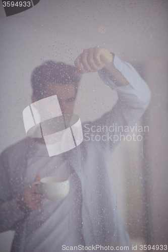 Image of relaxed young man drink first morning coffee withh rain drops on