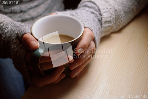 Image of Woman holds hot drink at a table under lamplight