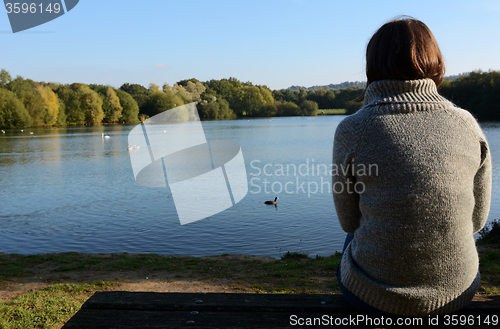 Image of Woman in a warm jumper sitting alone by a lake
