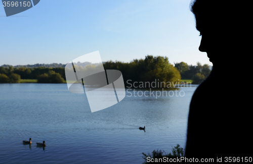 Image of Woman in silhouette sits beside a lake
