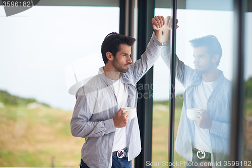 Image of relaxed young man drink first morning coffee withh rain drops on