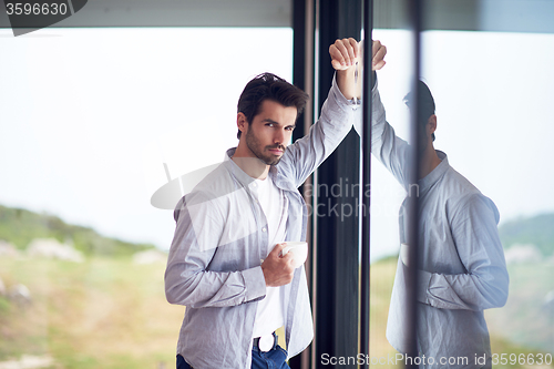 Image of relaxed young man drink first morning coffee withh rain drops on