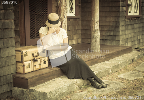 Image of Distressed 1920s Girl Near Suitcases on Porch with Vintage Effec