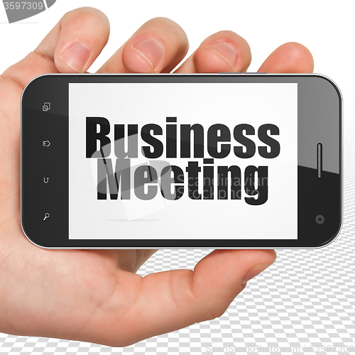 Image of Business concept: Hand Holding Smartphone with Business Meeting on display