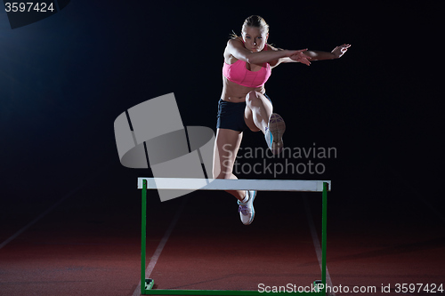 Image of woman athlete jumping over a hurdles