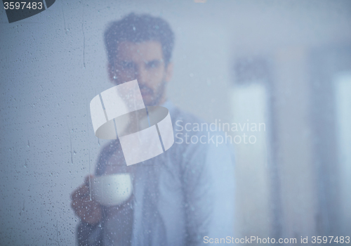 Image of relaxed young man drink first morning coffee withh rain drops on