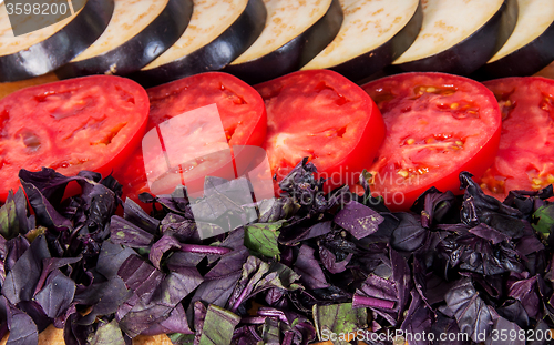 Image of Sliced eggplant tomato and basil leaves horizontally