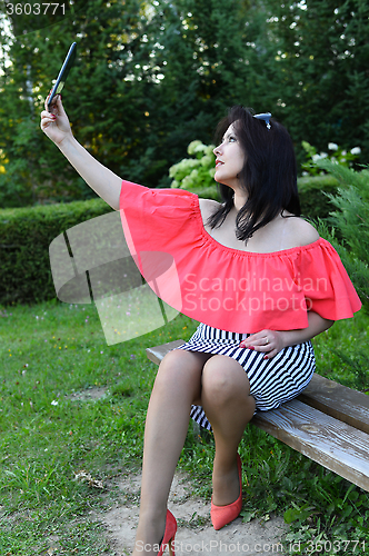 Image of Brunette girl sitting on a bench in the park with tablet