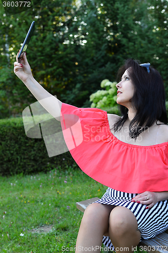 Image of Brunette girl sitting on a bench in the park with tablet