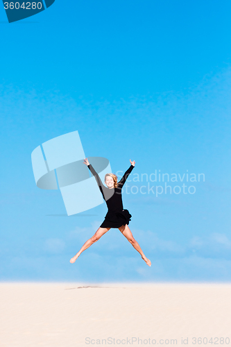 Image of Girl jumping in the air on sand dune.