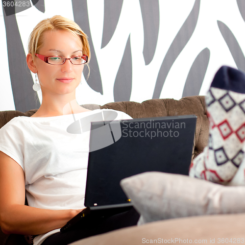 Image of Beautiful young lady sitting on sofa, using laptop.