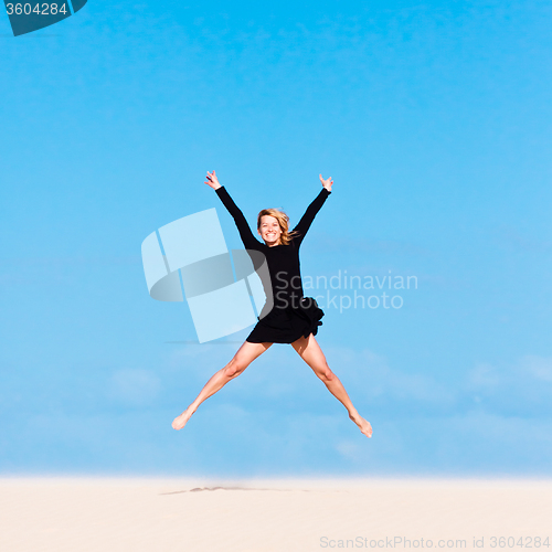 Image of Girl jumping in the air on sand dune.