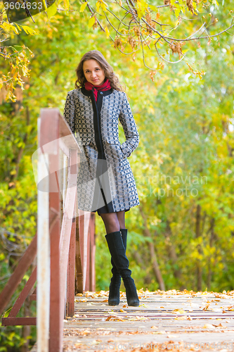 Image of Young girl leaned on the railing of the bridge against the backdrop of autumn leaves yellow