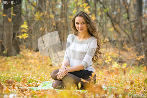 Image of Young beautiful girl sitting on a rug on the yellow fallen leaves