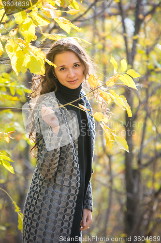 Image of Cute young girl holding a twig with yellow leaves against the backdrop of autumn yellow forest