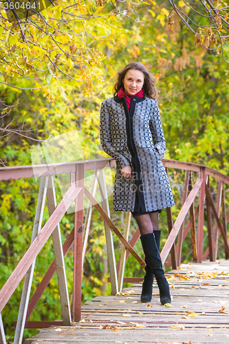 Image of Young girl leaned against the fence of the old bridge in the autumn forest