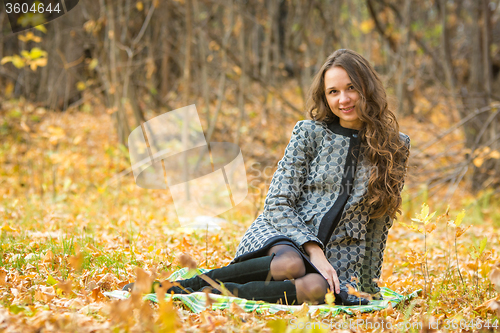 Image of Young beautiful girl in a yellow coat sitting on fallen leaves in the forest