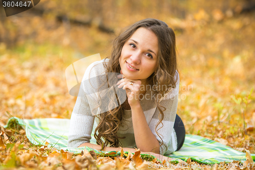 Image of Young beautiful girl lying on a rug in the autumn forest